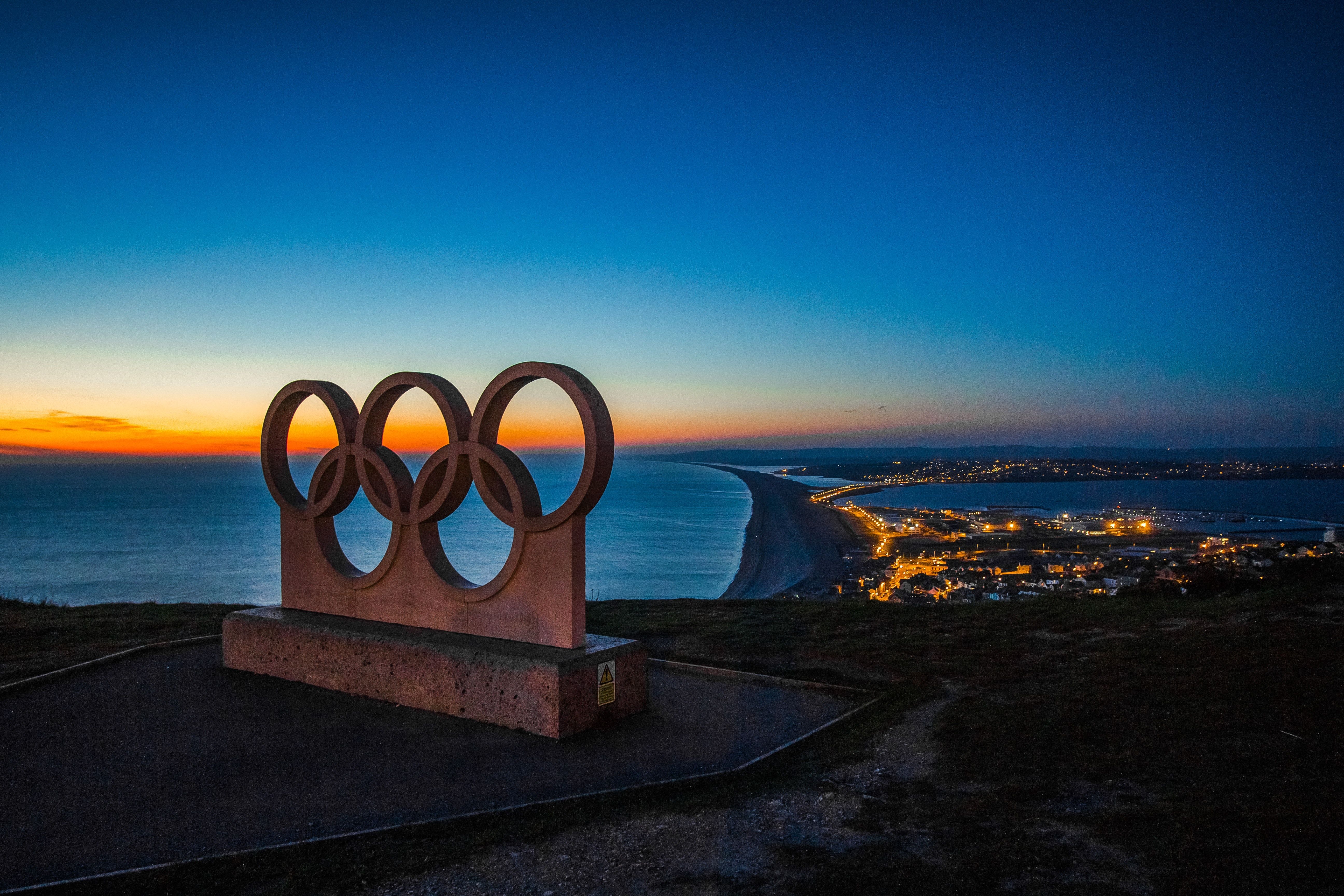 Olympic Rings carved in stone sit atop a pier overlooking the coastal city's lights below and the ocean