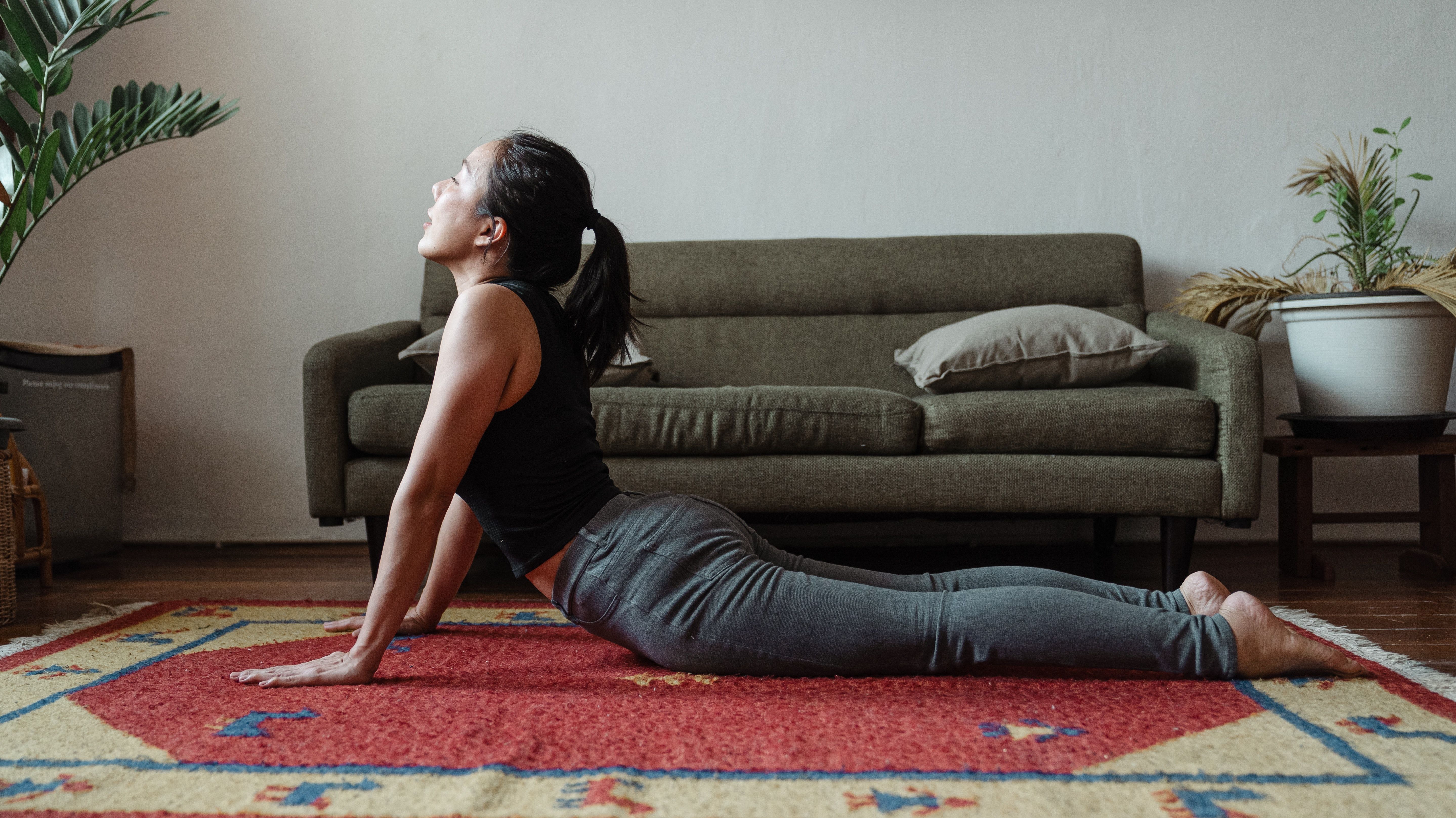 Woman performs cobra pose in front of couch